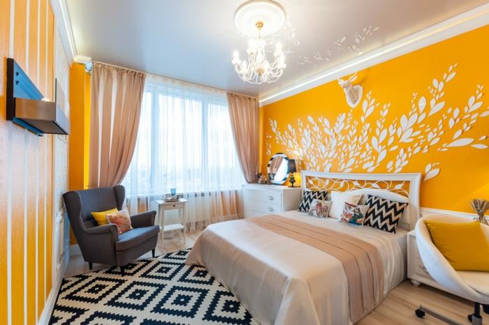 geltonos ir juodos spalvos miegamojo dekoras, „Chevron“ pagalvėlės, deimantinis kilimas, pilkas fotelis ir balta kėdė