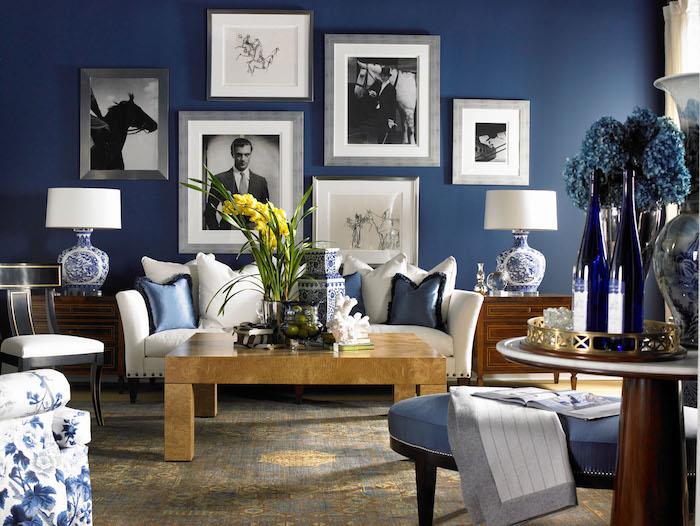 beli kavč in lesena mizica v dnevni sobi z modrimi stenami, črno -belimi okvirji za fotografije in risbami, modri poudarki