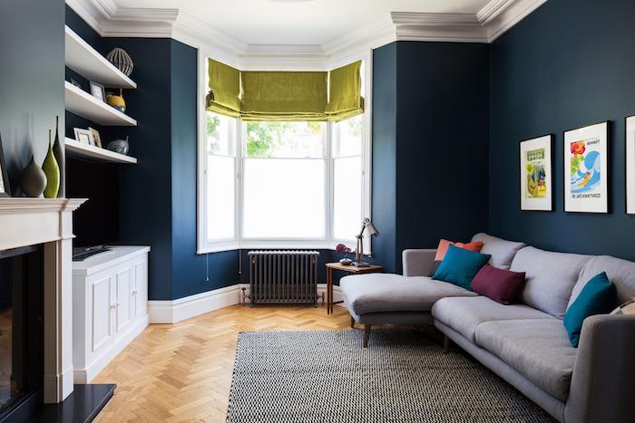 dolga postavitev dnevne sobe z modrimi stenami in sivim kavčem, okrašenim z barvitimi blazinami, belim kaminom, sivim radiatorjem