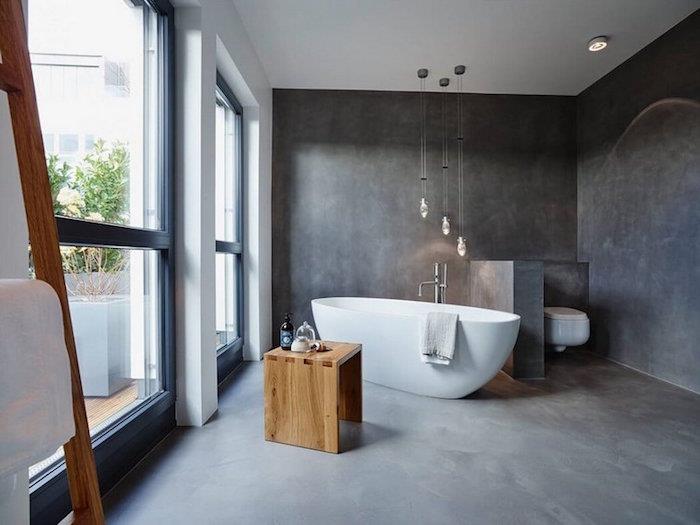 cilalı beton zeminli banyo ve duvarları beyaz bağımsız küvet ve ahşap tabure, bölme duvarlı tuvalet alanı
