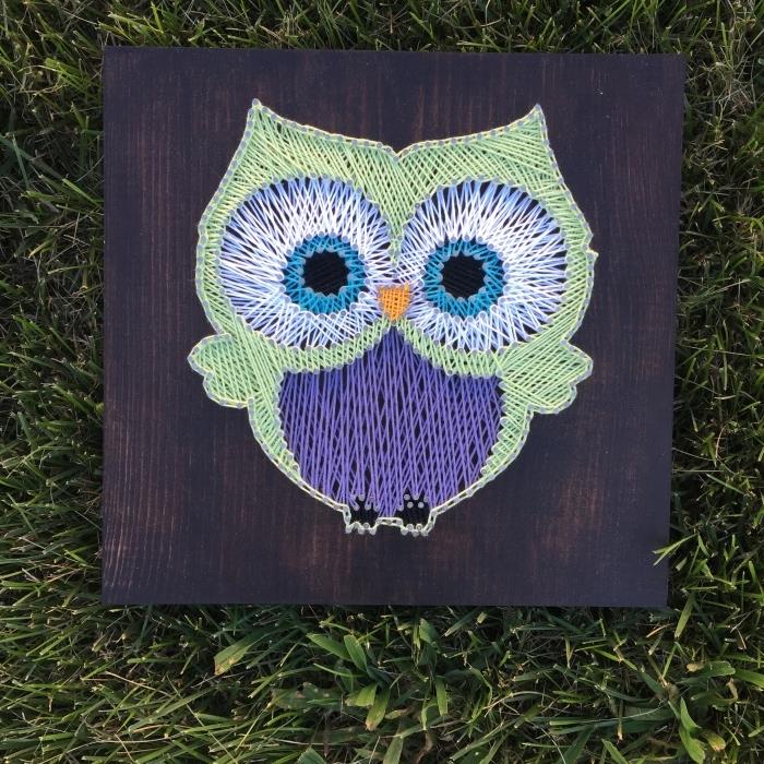mielas kūrinys ant tamsios medienos lentos, žalios ir violetinės pelėdos dizaino su didelėmis mėlynomis akimis