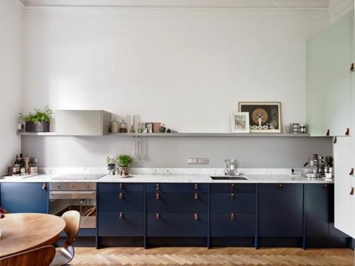 erdvi šviesiai pilka virtuvė su tamsiai tamsiai mėlynos spalvos spintelėmis, šviesiai smėlio spalvos laminato grindimis, apvaliu mediniu stalu ir atitinkamomis kėdėmis
