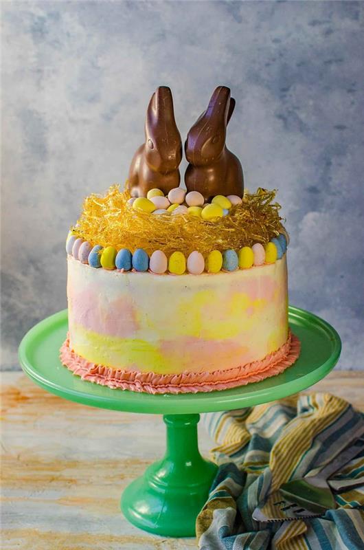 prav posebna velikonočna torta s prelivom v rožnati in rumeni barvi, okrašena z velikonočnim gnezdom s karamelo in dvema čokoladnima zajčki