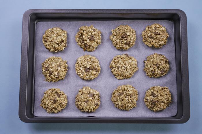 recept za čokoladne piškote, ovseni kosmiči, razporejeni na belem pekaču, v pekaču, modra miza