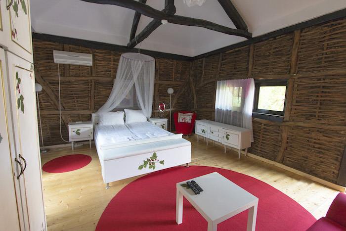 dekor spalnice, okrogla malinova preproga, postelja z baldahinom, bela omara s cvetličnim okrasjem, stol iz rdeče tkanine