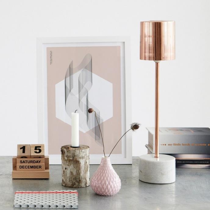 pilka stalo apdaila su baltu nuotraukų rėmeliu su rožiniu raštu ir šviesiai rožine origami dizaino vaza, vario stalinės lempos modelis su betono dizaino atrama