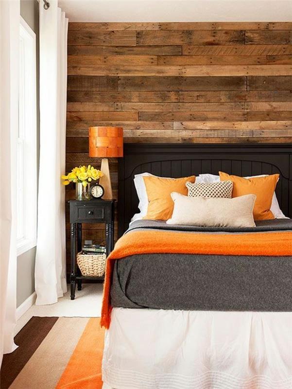 šiltos medinės lentos, ant miegamojo sienos, priešingoje sienoje yra pilka, tamsiai pilka lova, šviesiai pilka ir smėlio spalvos, o oranžiniai lovatiesės ir pagalvės, spalvos, derančios prie pilkų sienų, dryžuotas trijų tonų kilimas