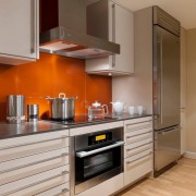 Oranžinė prijuostė kartu su baltais ir pilkais atspalviais virtuvės interjere