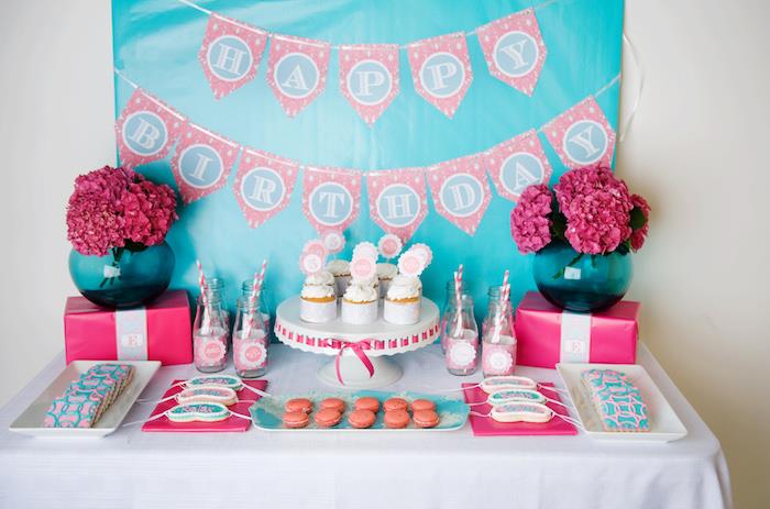 SPA tematikos rožinės ir mėlynos spalvos saldainių baras su fuksijos gėlių puokštėmis, keksiukais, makaronais, dekoruotais sausainiais