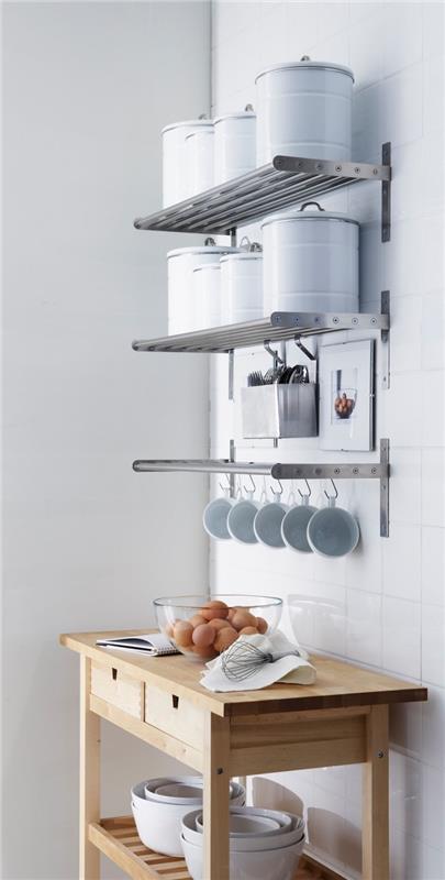pramoninio stiliaus sieninė virtuvės spinta iš nerūdijančio plieno, sieninės lentynos puodams ir kavos puodelio laikiklio juosta su kabliukais, šviesaus medžio serviravimo vežimėlis su stalčiais ir lentynomis