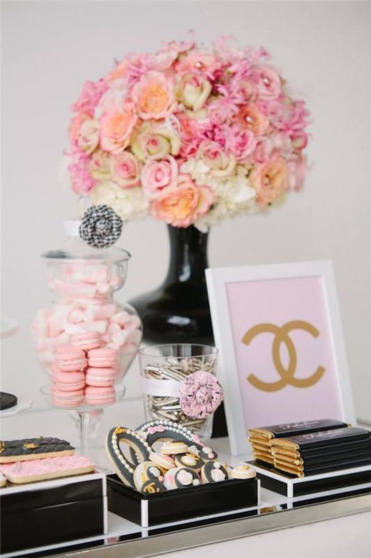 gėlių puokštė juodoje vazoje, cukruoti migdolai, juodos ir rožinės spalvos makaronai ir sausainiai, juodos ir auksinės spalvos šokoladas