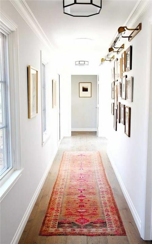 orientalska večbarvna preproga, na lesenih tleh, v belem hodniku, ideje za oblikovanje hodnika, z okni in številnimi uokvirjenimi podobami