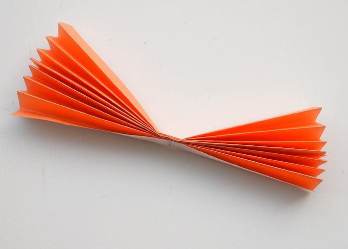 Un pezzettino di carta arancione piegato a fisarmonica e fissato con un nastro adesivo