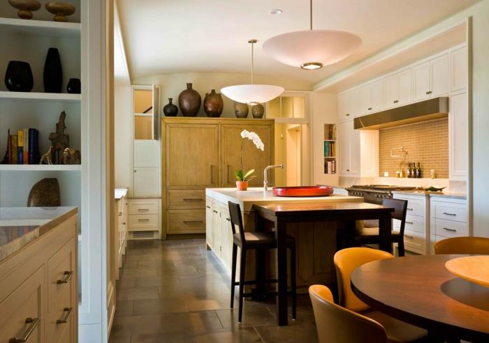 maža tradicinio dizaino virtuvė, balta virtuvės sala, apvalus medinis stalas, geltonos kėdės, medinė spintelė ir moliniai puodai