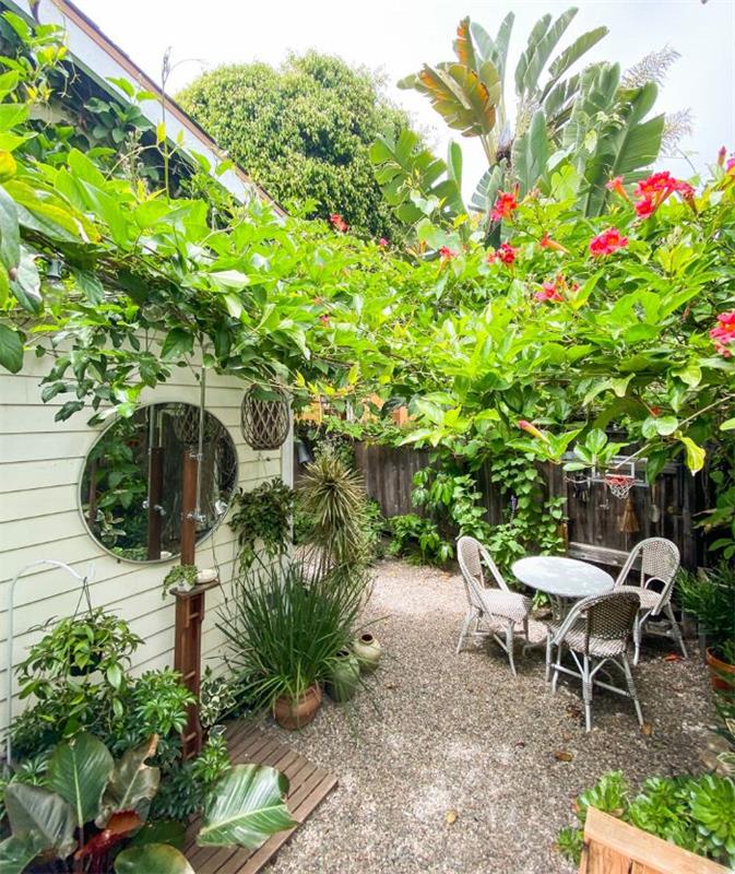 lesena ograja s tropskimi rastlinami okoli jedilnih stolov in okrogle mize v lončkih z vrtnim gramozom
