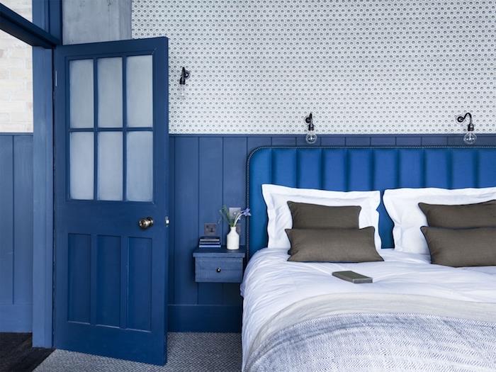 modre stene in vrata, sivo -belo posteljnina na postelji z modrim vzglavjem, sivo -bela preproga, vintage barve v barvi dekor dnevne sobe