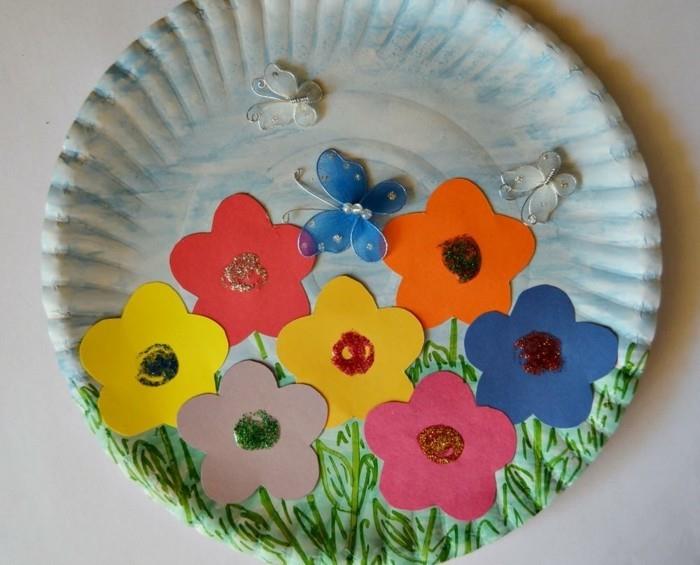 umetniški projekti diy, plošča iz belega papirja, okrašena z modro-zeleno barvico, barvitimi izrezi v obliki rož in majhnimi okraski iz metuljev
