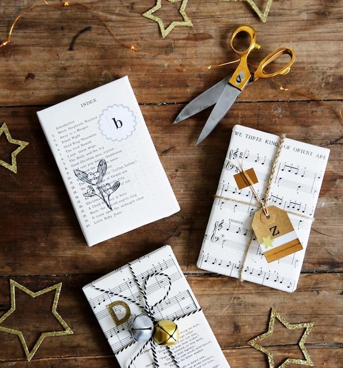 Kalėdinių dovanų įvyniojimo pavyzdys, natų popierius, ryšuliai, perrišti virvele ir varpelių bei dovanų etikečių puošmena