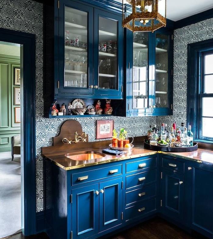 modro -bele kuhinjske tapete s cvetličnim vzorcem, visoka in nizka kuhinjska omara modre barve in lesena delovna plošča, starinski lestenec