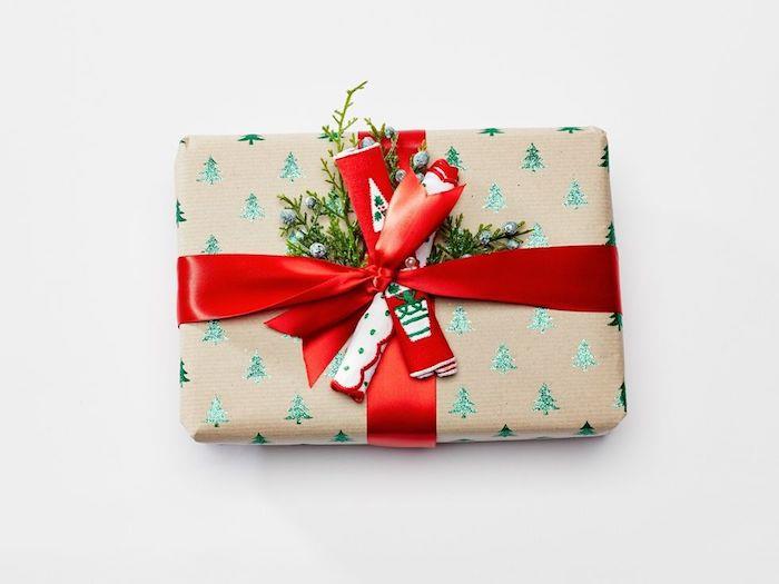 Ideja o božičnem darilu v kraft papirju z zelenimi vzorci božičnega drevesa, rdečim trakom in zelenimi vejami