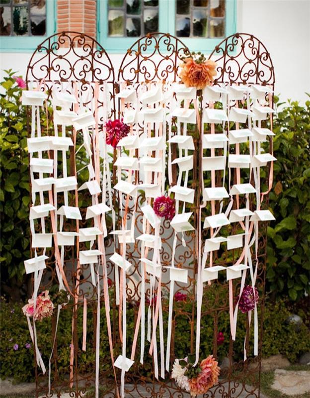kapılar, barok tarzı metal ızgara, beyaz ve pembe kurdeleler ile dekorasyon, çiçek açan çiçekler ve beyaz etiketler ile diy düğün masası planı