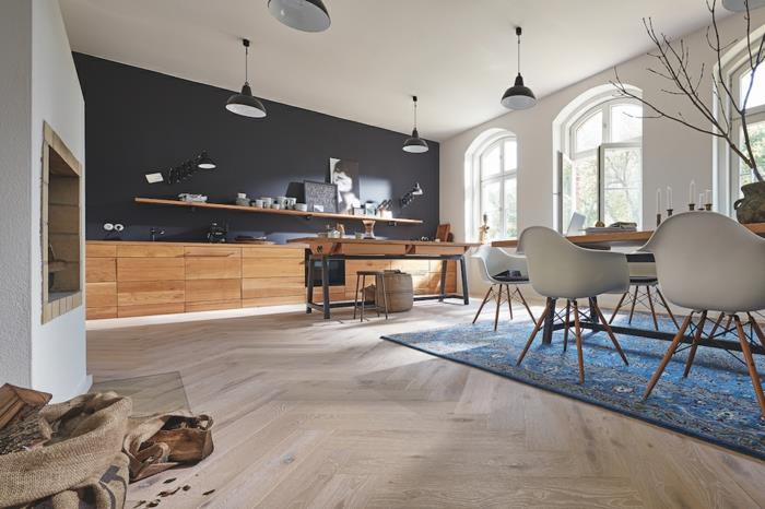 didelė virtuvė, kietmedžio virtuvės grindys, mėlynas kilimas, juoda siena, medinės spintelės, pramoninės lempos, arkiniai langai