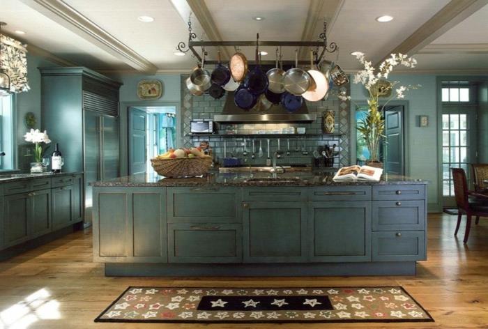 tradicinio dizaino virtuvė, autentiškos parketo virtuvės grindys, pakabinami indai, mėlynai dažytos spintelės, centrinė sala, kilimai