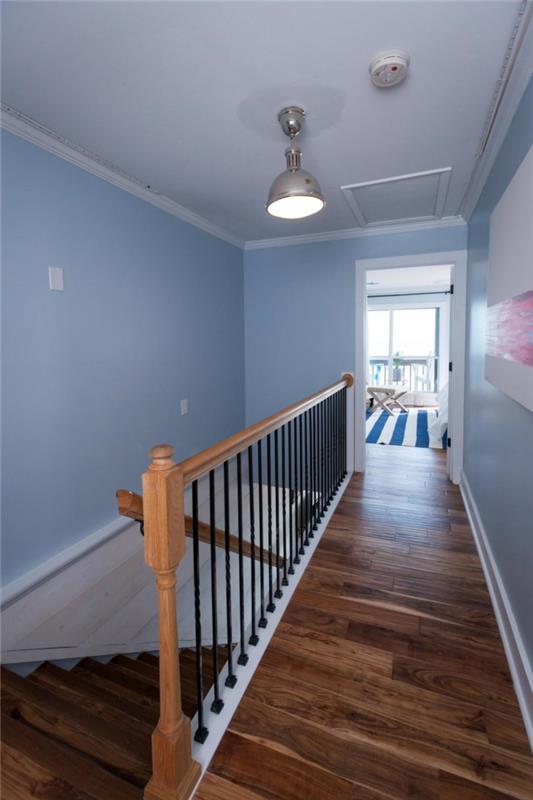pristanek z bledo pastelno modrimi stenami in belim stropom z navadno svetlobo, lesena tla in ograje, dekor na hodniku, okvirjena slika z belo in roza barvo