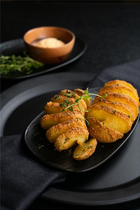 Potato hasselback, piatto con patate al forno cosparse con del timo freska