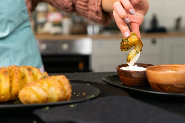 Patata a fisarmonica immersa in una ciotola con maionese, piatto con patate al forno