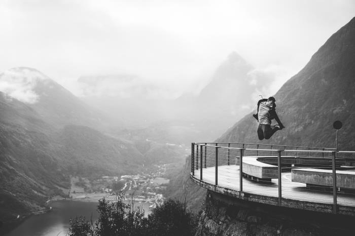 moški, ki skače po ozadju veličastnih gora in doline, črno -beli portret človeka in narave