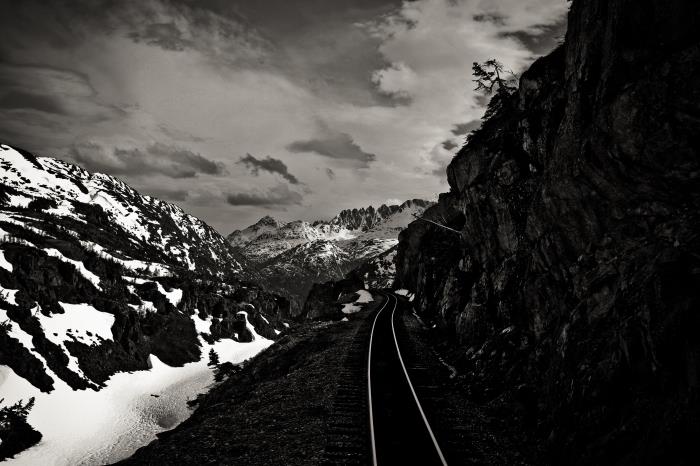 črno -bela fotografija železnice v zimski gori, ki se prepleta med skalami