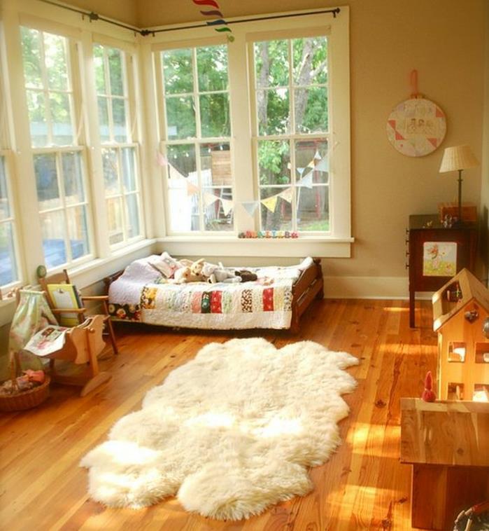 medinis parketas, baltas kilimas, montessori kūdikio lova ant grindų, maža kėdė, mediniai žaidimų namai, smėlio spalvos siena, montessori metodas