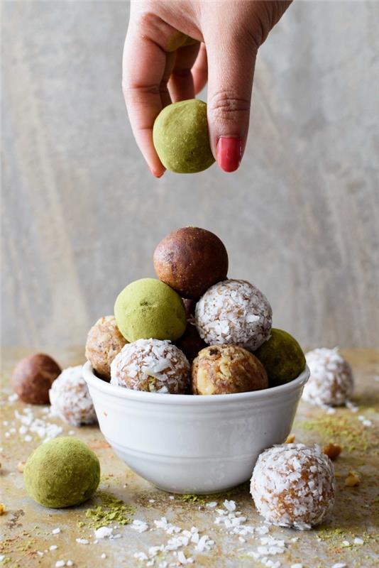 moteriška ranka su rožiniu nagų laku, žemės riešutų sviesto avižų rutuliukais, padengta kokoso drožlėmis, matcha milteliais, baltame dubenyje
