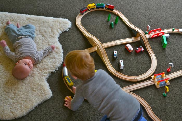 soba montessori, bela živalska koža s kratkim plaščem, otrok, ki se igra z vlaki in otroško plenico, ki ga opazuje, zgodnje učenje igre, učenje gibanja