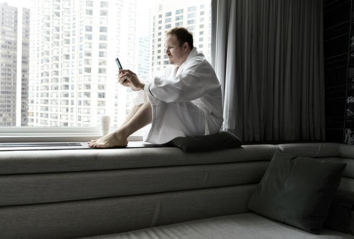 telefonu, gri mobilyaları, gri perdeleri ile pencere kenarında oturan bir adam