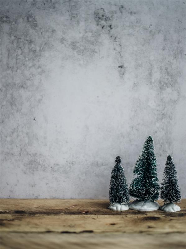 Minimalistinė Kalėdų tapetų idėja išmaniajam telefonui, mini snieguotų eglutės figūrėlių nuotrauka priešais betoninę sieną