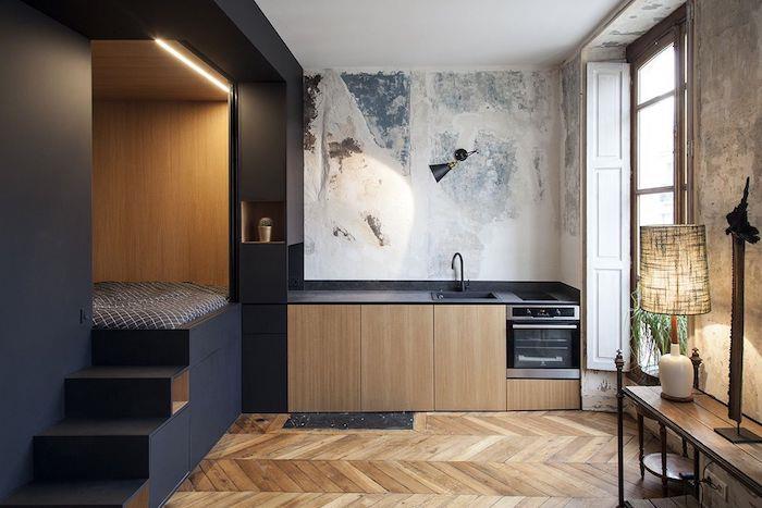 20 m2 studijos išdėstymas su juodos ir medinės virtuvės bei miegamojo erdve ant juodos nišos platformos, šviesaus medžio parketas