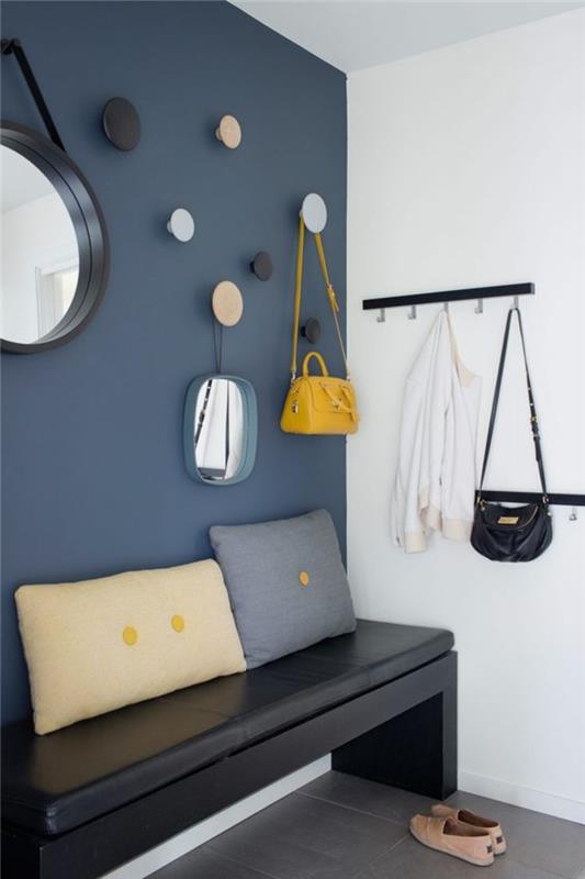 anties mėlyni dažai ant sienos, kabliai juodos, mėlynos ir pastelinės rožinės spalvos, suoliukas iš juodos dirbtinės odos, didelis apvalus raganos veidrodis, mažas veidrodis, metaliniai kabliai iš juodo metalo, taupe grindys, stačiakampė pagalvė smėlio spalvos su dviem geltonais taškeliais , mėlyna kvadratinė pagalvėlė su geltonu tašku