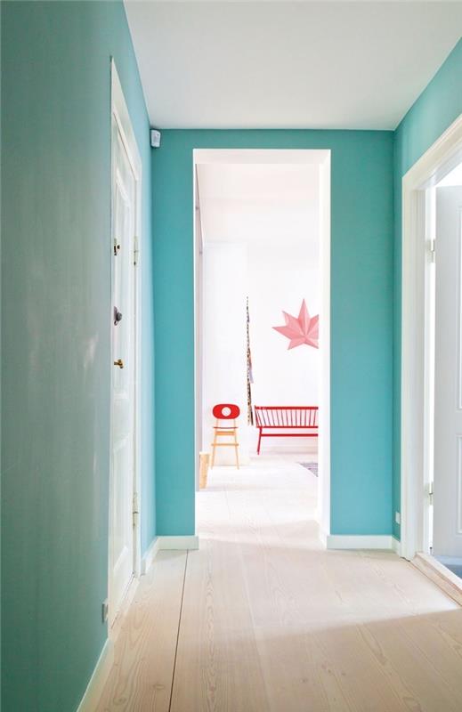 turkizno modra stena se popolnoma ujema z belimi vrati in svetlim parketom, da ustvari sodobno in pomirjujoče vzdušje na hodniku