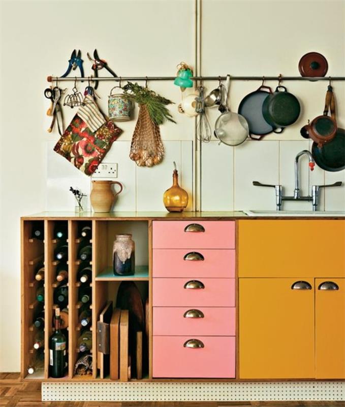 perdažykite virtuvės spintelę, virtuvės spinteles ir stalčius, perdažytus ochros geltonos ir pastelinės rožinės spalvos, medinio vyno butelių laikymo ir indų laikiklio vamzdelį