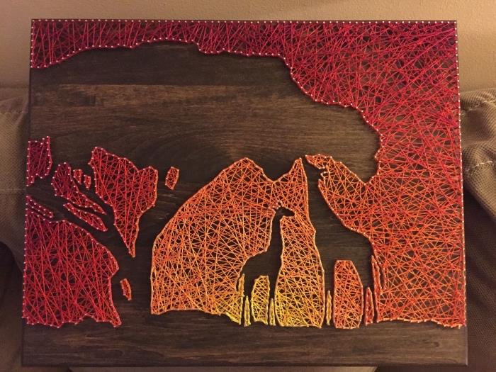 gražus kūrinys Afrikos tema su tamsia medine lenta ir saulėlydžio kraštovaizdžiu bei žirafomis siuvimo siūlu