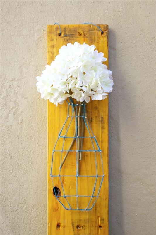 graži dekoratyvinė vaza mėlynais siūlais ir baltomis gėlėmis pripildytos vinys ant geltonos spalvos medinės lentos
