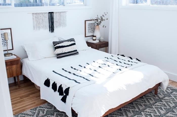bela spalnica z lesenimi tlemi z veliko geometrijsko oblikovano preprogo in nočno omarico iz temnega lesa