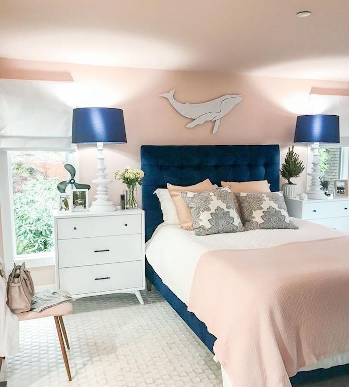 stene v barvi lososa v spalnici s talnimi svetilkami in modro posteljo, beli predalnik, bela preproga, barvni trend 2020 klasično modra