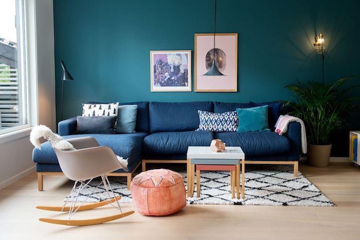 kavč v klasični modri barvi in ​​stena v pavovi modri barvi v skandinavski dnevni sobi s skandinavskim gugalnikom, lososovim pufom, črno -belo preprogo