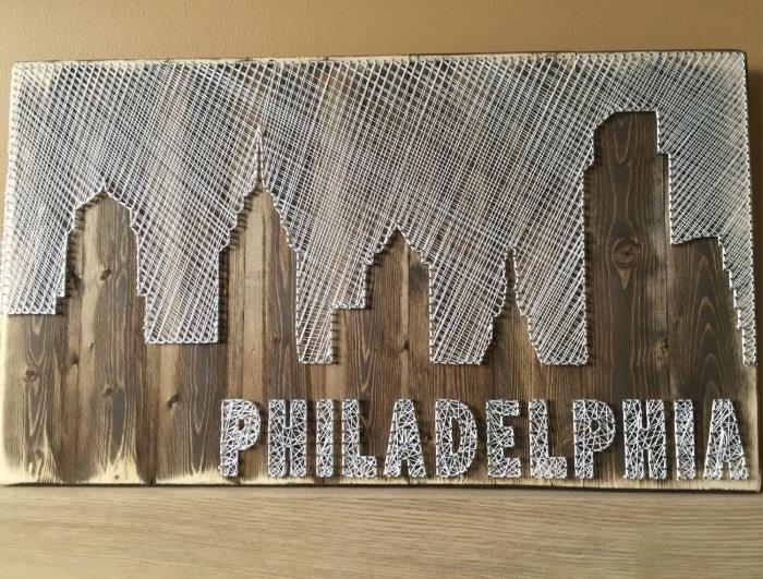kūrybinių pomėgių idėjos su medine ir balta viela, tamsaus medžio lentos šablonu ir balta viela miesto pavidalu su raidėmis Filadelfija
