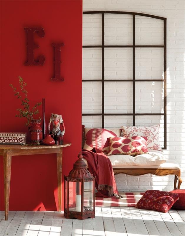 ženska dekoracija spalnice z rdečimi stenami, notranje oblikovanje v slogu etničnega stila z lesenimi predmeti, prijeten kotiček z blazinami in preprogo v beli in rdeči barvi