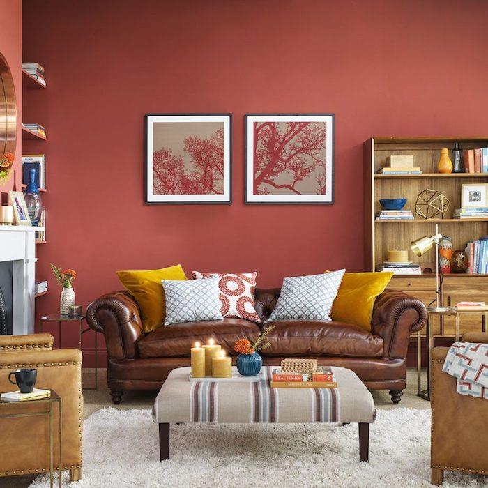 rdeča barva na steni v dnevni sobi, moderna z rumenimi poudarki, usnjeni kavč in naslanjači z rumeno -belimi blazinami, bela preproga, lesena knjižna omara, romantičen dekor, kamin