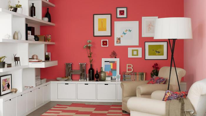 çerçeveler ve dekoratif aksesuarlar, kitaplık ve beyaz depolama mobilyalarının zengin duvar dekorasyonu ile modern bir oturma odasında somon pembesine eğilimli kırmızı boya